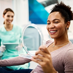 Woman smiling while looking at reflection in handheld mirror