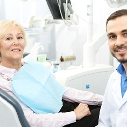 A male dentist smiling while seated next to an older female patient who is receiving necessary care using her dental insurance in Arlington