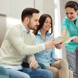 A dental receptionist giving a man and woman information about the services provided and cost