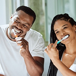 Couple smiling while brushing their teeth at home