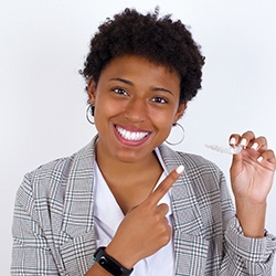 Young woman pointing to Invisalign aligner in hand