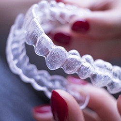 Woman holding Invisalign aligner on dark background