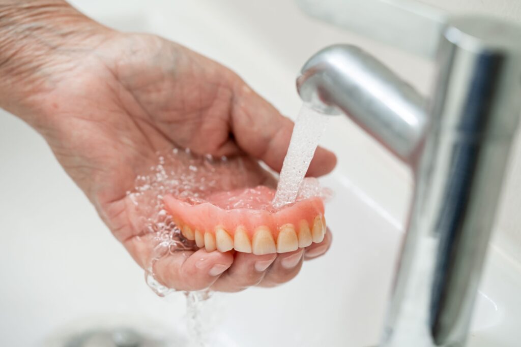 Hand holding dentures under running tap water